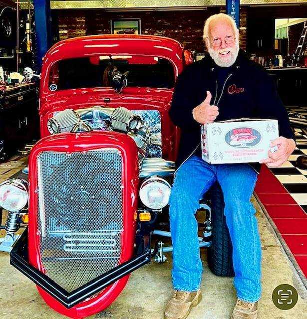 Boss Hog founder holding a torque converter beside a red hot rod